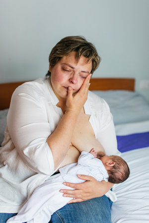 Mother breastfeeding her newborn son while crying on bedの写真素材