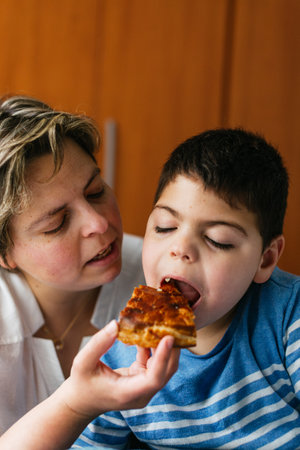 Mother feeding her son with disability a slice of pizza at homeの写真素材