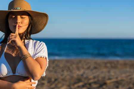 Calm chinese woman making silence gesture on beach at sunsetの写真素材