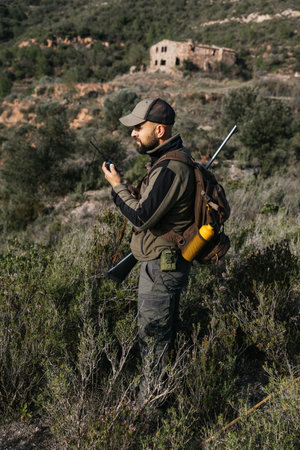 Hunter using walkie talkie with rifle on shoulderの写真素材