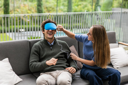 Couple relaxing on sofa, woman placing sleep mask on manの写真素材