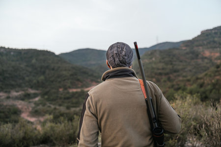 Hunter wearing khaki looking at valley with rifleの写真素材
