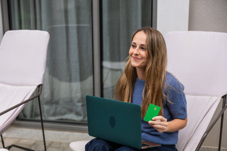 Young woman shopping online using laptop and credit card on patioの写真素材