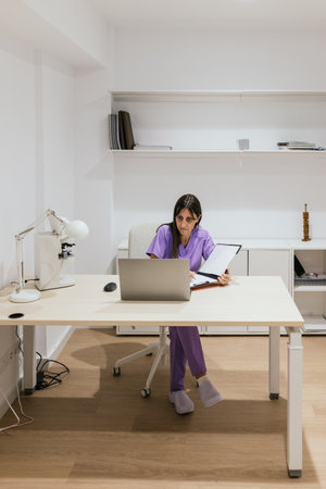 Optometrist working with laptop sitting at desk in her officeの写真素材