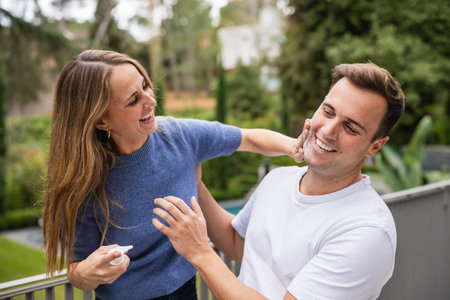 Playful couple applying sunscreen or exfoliating cream on balconyの写真素材