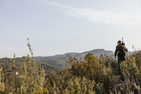 Hunter walking in the mountains with rifle on shoulderの写真素材