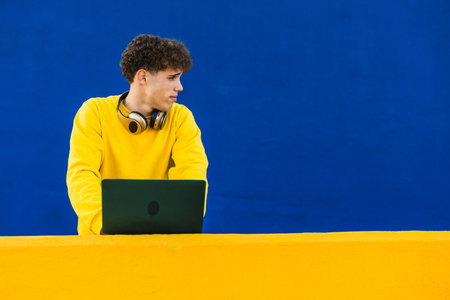 College student using laptop with headphones around neck and looking away