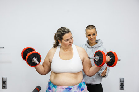 Personal trainer supporting client lifting weights in gymの写真素材