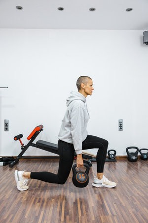 Determined sportswoman performing kettlebell lunges in home gym, building strength and fitness...