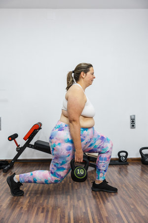 Overweight woman doing kettlebell stride training in gym