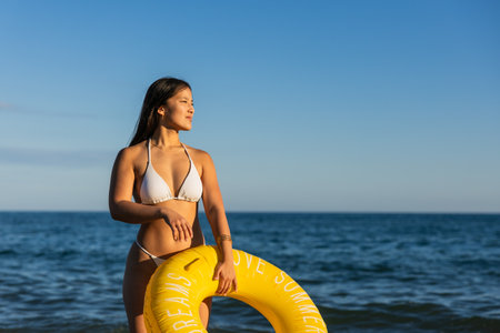 Young chinese woman holding inflatable ring at beach enjoying summer vacationの写真素材