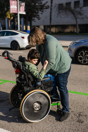 Mother placing child in wheelchair in parking lotの写真素材