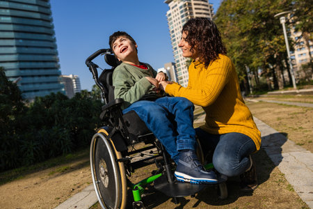 Mother playing with son in wheelchair in city parkの写真素材