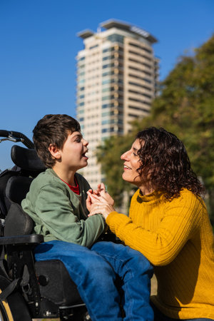 Mother holding hands with son in wheelchair, sharing a moment of love and careの写真素材