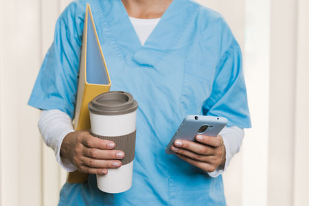 Nurse using smartphone and holding coffee and folderの写真素材