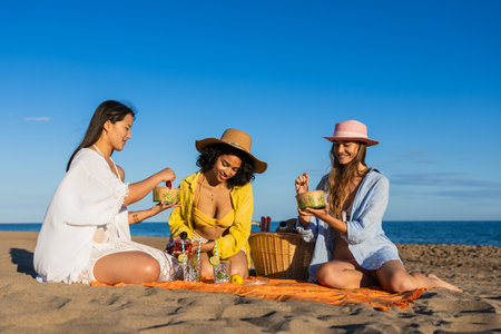 Multiethnic women friends eating healthy food at beach picnicの写真素材