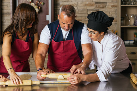 Chef teaching couple how to roll dough during cooking classの写真素材