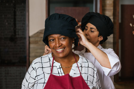 Professional chef helping trainee wearing chef hat in restaurant kitchenの写真素材