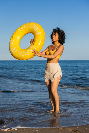 Young latin woman holding inflatable ring at beach during summer vacationの写真素材
