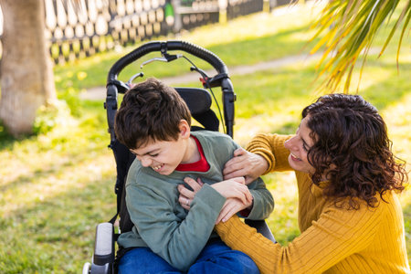 Happy mother playing with son in wheelchair outdoorsの写真素材