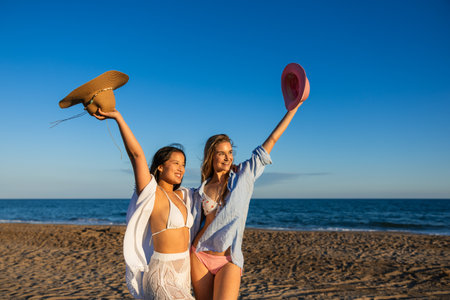 Happy women raising hats on beach enjoying summer vacationの写真素材