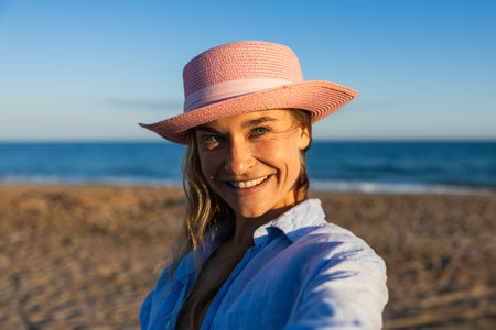 Happy tourist wearing pink hat enjoying sunny beachの写真素材