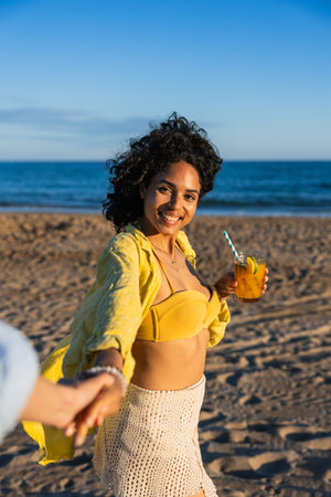 Happy young woman holding hand and drinking cocktail on the beachの写真素材