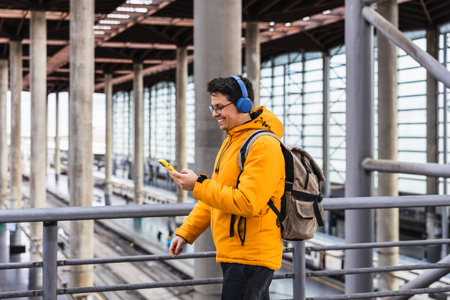 Traveler wearing headphones listening to music and using smartphone in train stationの写真素材