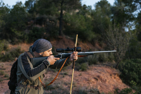 Hunter aiming with rifle in forest at sunsetの写真素材