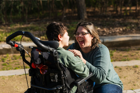 Mother having fun with son with disability in wheelchair in park