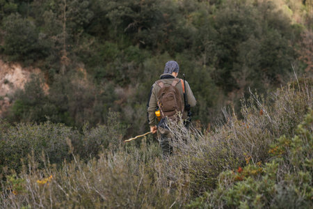Hunter walking through forest carrying rifle and backpackの写真素材