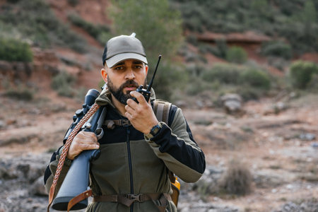 Hunter using walkie talkie while holding rifleの写真素材