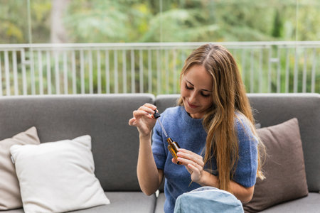 Woman applying essential oil from a dropper bottle at homeの写真素材