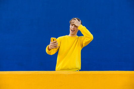 Surprised college student reacting to news on smartphone against colorful backgroundの写真素材