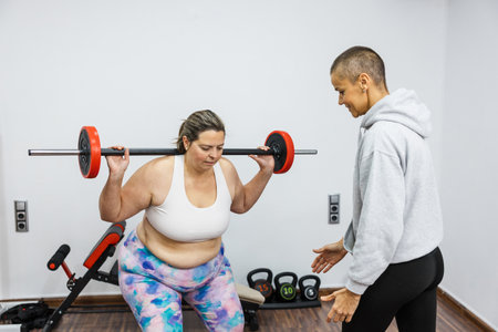 Personal trainer guiding client during weightlifting squat exerciseの写真素材