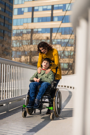 Mother comforting son with disability in wheelchair on bridgeの写真素材
