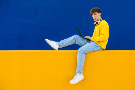 College student using laptop sitting on colorful wallの写真素材