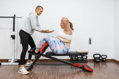 Personal trainer supporting overweight client doing sit ups in gymの写真素材