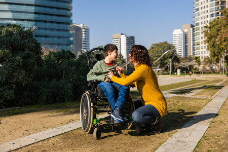 Mother playing with son with disability in wheelchair in city parkの写真素材