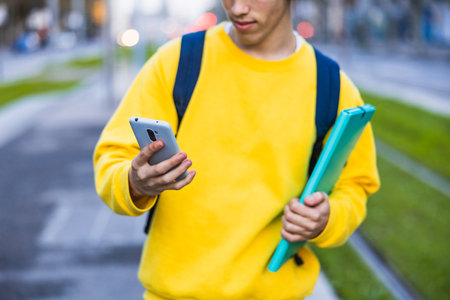 College student using smartphone and holding books in campusの写真素材