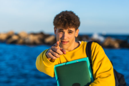 College student pointing finger holding book by the sea