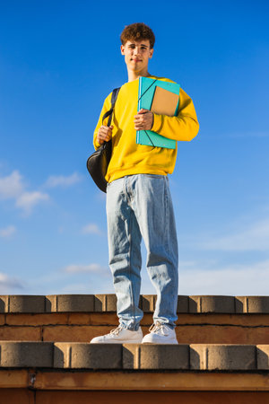 College student holding folders and backpack standing on steps on sunny dayの写真素材