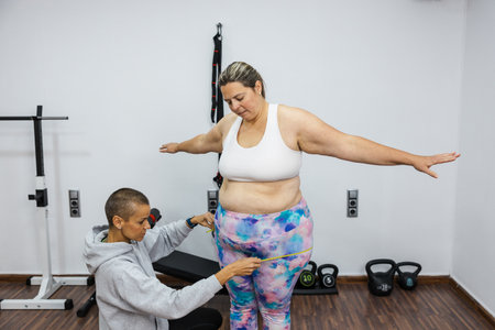 Nutritionist measuring waist of overweight woman in gymの写真素材