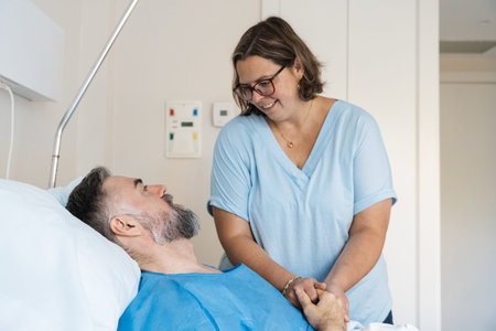 Woman visiting patient holding his hand in hospitalの写真素材