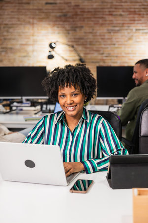 Smiling black businesswoman working on laptop in modern officeの写真素材