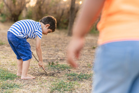 Boy exploring ground with stick barefoot outdoorsの写真素材