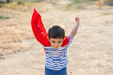 Little boy playing superhero flying with red capeの写真素材