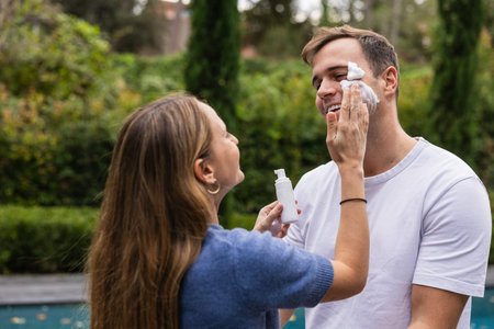 Woman applying exfoliating foam on mans face outdoors