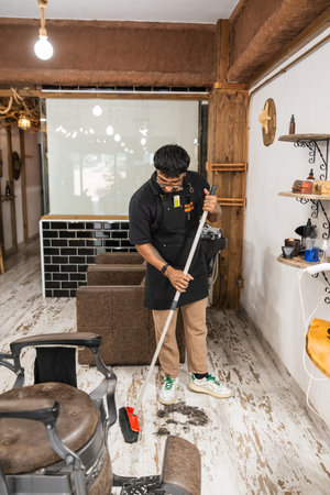 Barber sweeping hair from barbershop floor