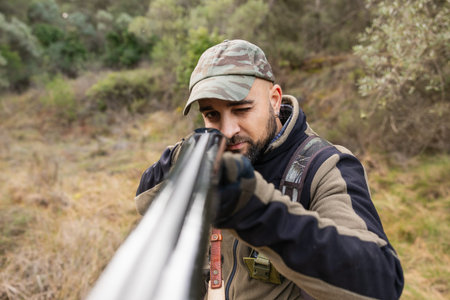 Hunter aiming shotgun while stalking prey in nature